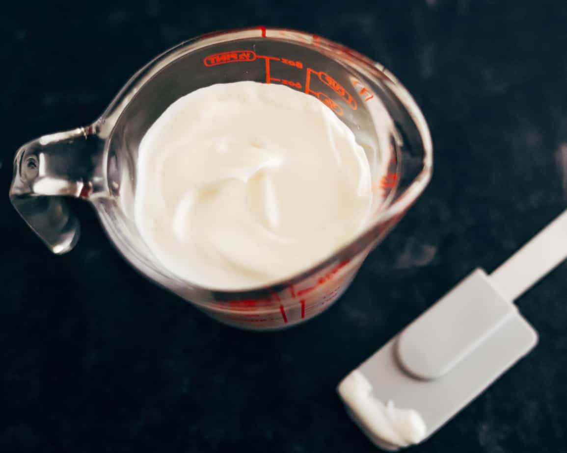 Glass measuring cup filled with buttermilk and mayonnaise for making Ranch dressing