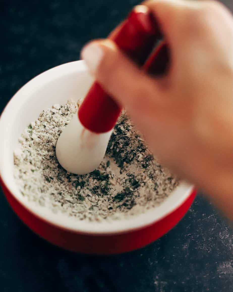 Red Pestle grinds and stirs together spices and herbs in a porcelain mortar to crush seasoning into a fine texture