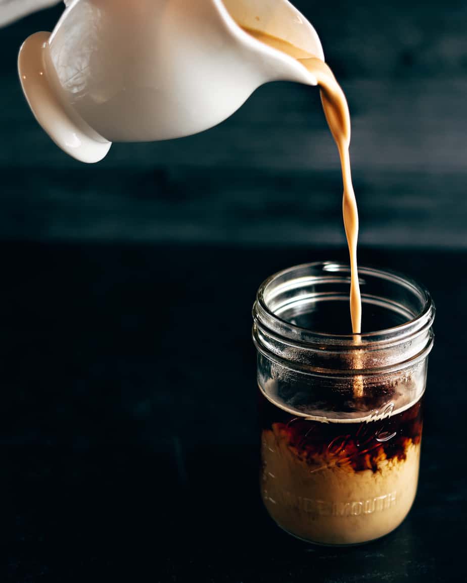 White porcelain creamer pours coconut milk creamer into a mason jar of coffee