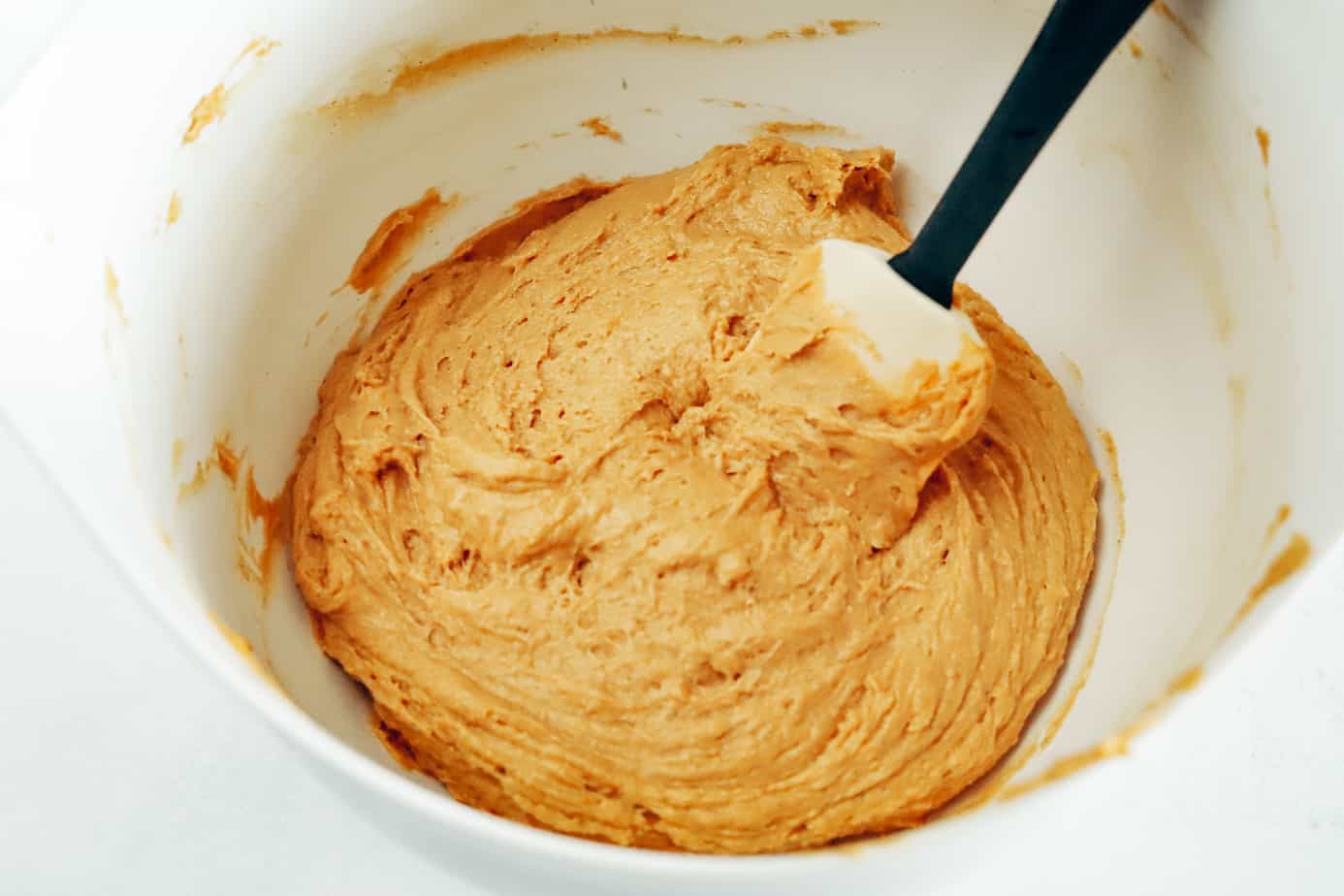 Bowl of pumpkin cookie batter being mixed with a rubber spatula
