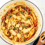 Dutch oven with papardelle pasta tossed in slow cooked bolognese and green peas