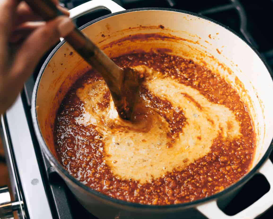 Stirring cream into a braised bolognese counter clockwise before letting the sauce simmer