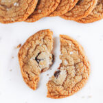 Soft and chew brown butter cookie is broken in half, exposing the dark chocolate chunks and smoked sea salt flake garnishes.