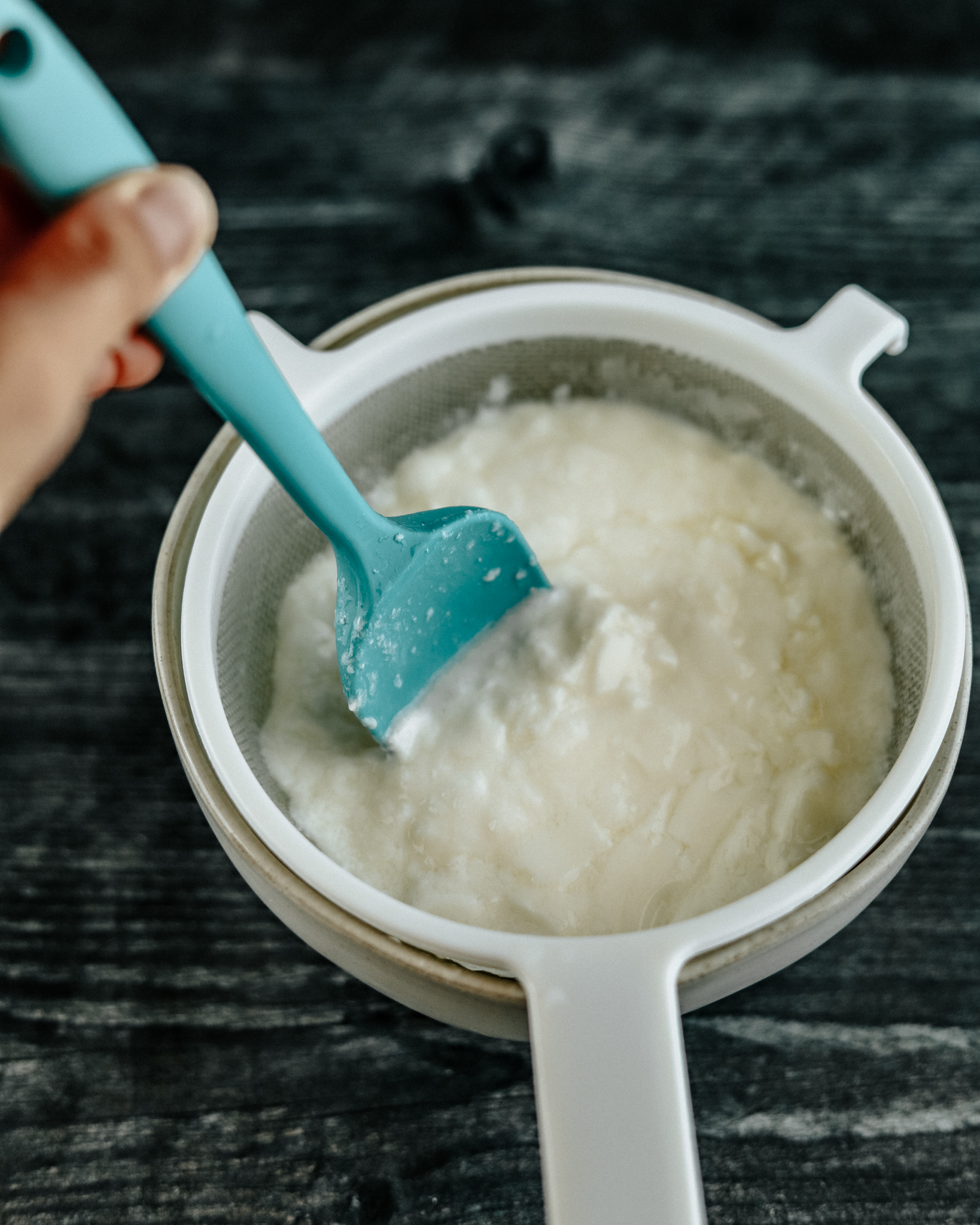 Silicone spatula separates kefir from grains in a white mesh strainer