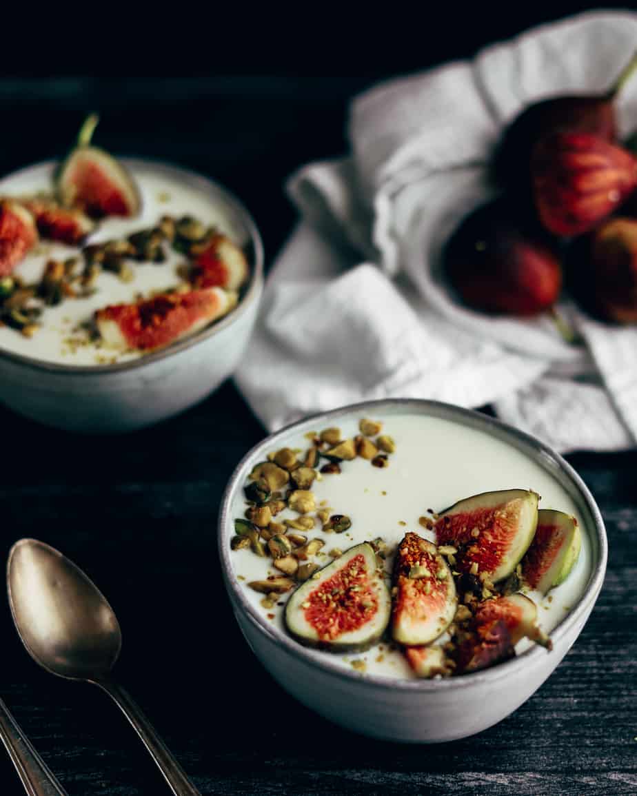 Bowl of kefir parfait topped with fresh figs and crushed raw pistachios