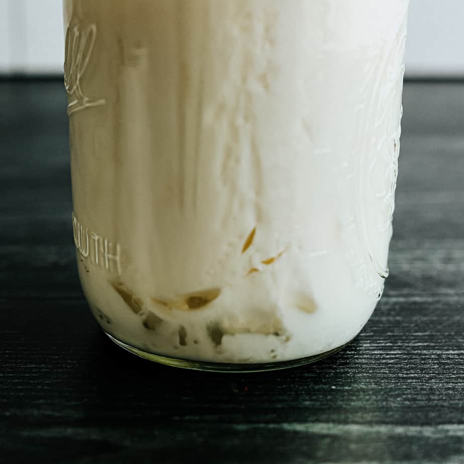 glass jar of kefir with pockets of whey beginning to separate, indicating that it's ready to be strained.