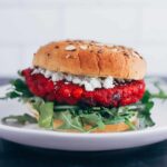 A beet burger is plated and garnished with goat cheese, arugula, topped with a seeded bun.