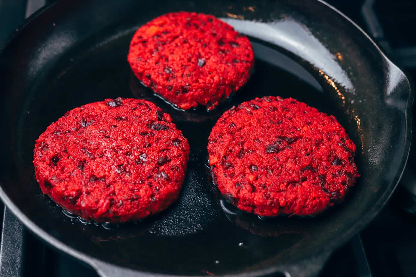 Veggie burgers grilling over olive oil in a cast iron skillet.