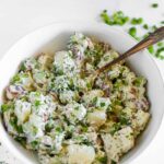 Bowl of red potato salad garnished with bright green chopped dill weed.