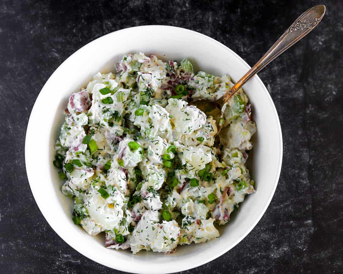 Bowl of red potato salad garnished with bright green chopped dill weed.