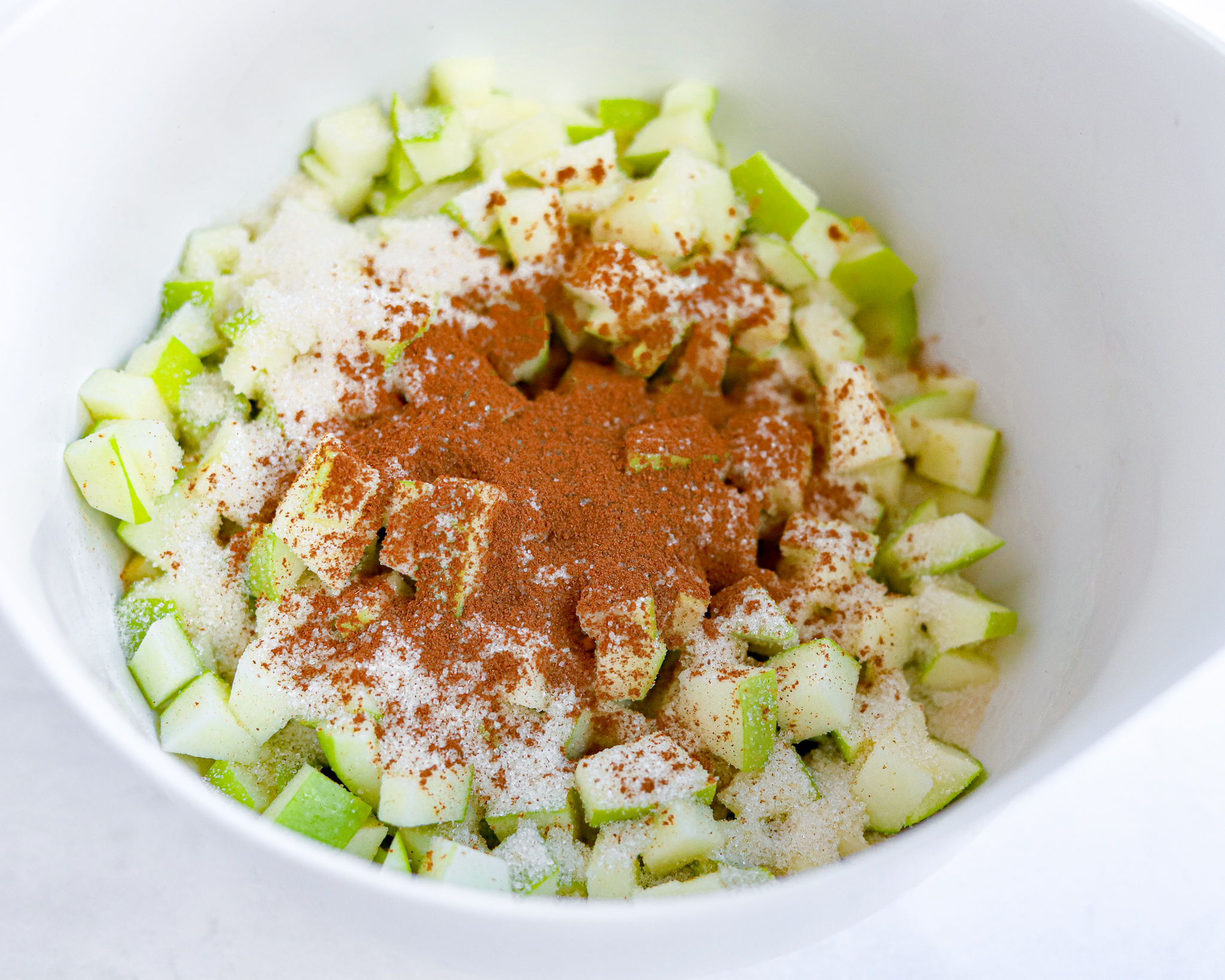 Bowl of green apples diced and covered with a heap of sugar and cinnamon spices before being baked.