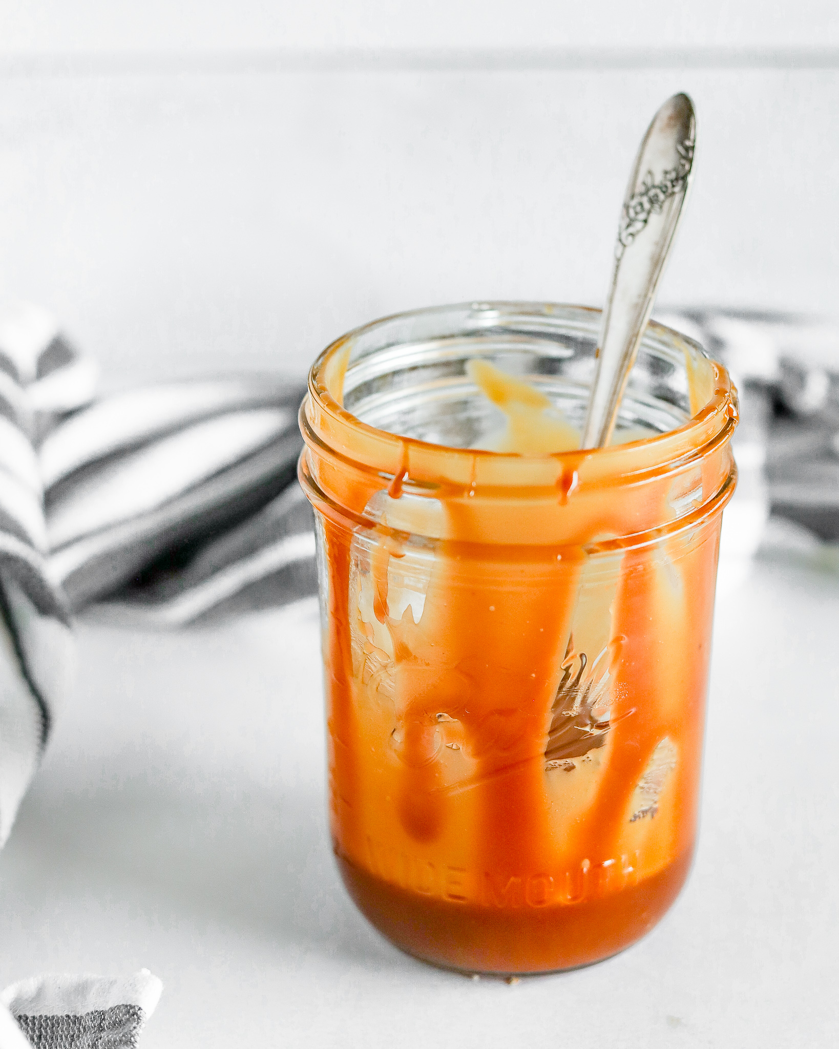 ball jar of caramel with a vintage spoon inside and caramel dripping down the jar
