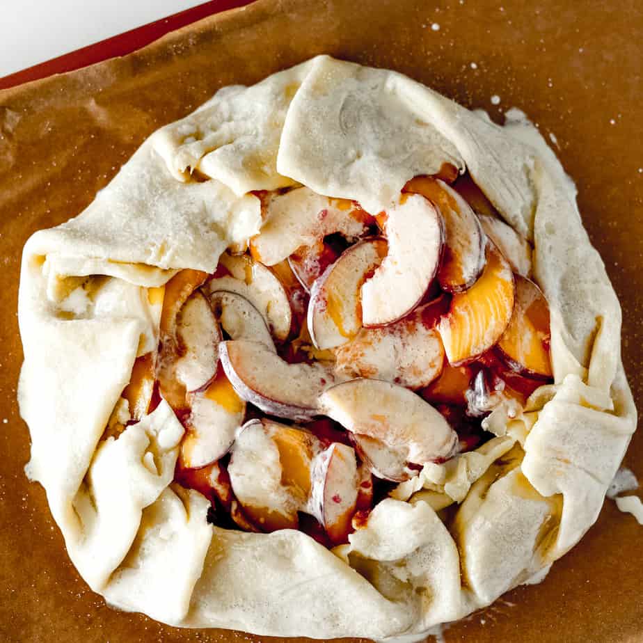 Sliced peaches wrapped in pie dough and brushed with heavy cream before baking a galette
