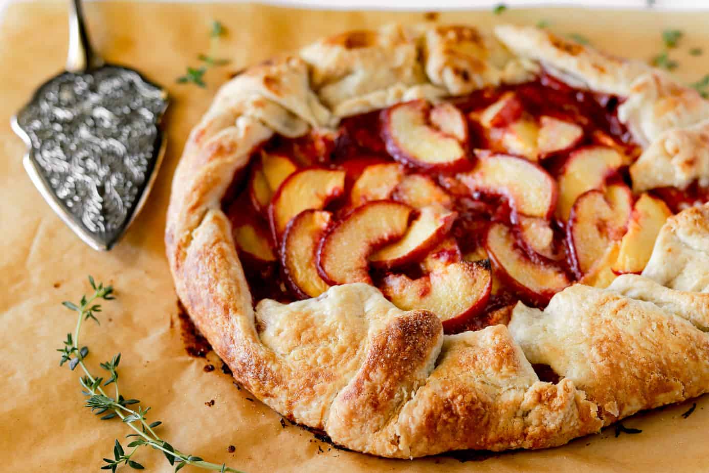 Close of up a peach galette freshly baked with a vintage silver cake server next to it