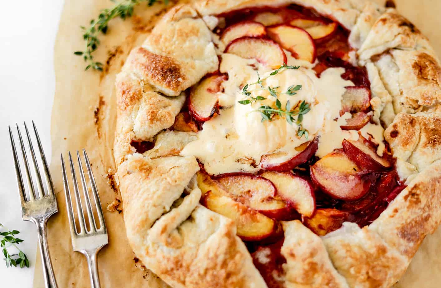 Fresh thyme sprigs over a peach galette topped with vanilla ice cream that's beggining to melt into the peaches