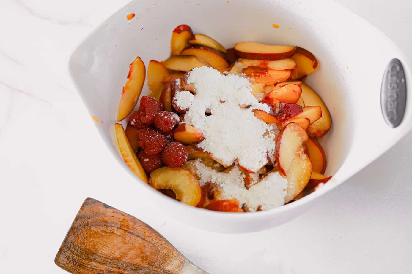 Bowl of sliced peaches and raspberries tossed in a scoop of sugar