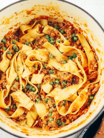 tagliatelle pasta is tossed in bolognese with sausage and peas inside of a white cast iron dutch oven