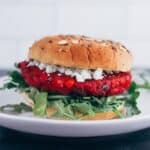 beet burger topped with arugula, goat cheese, and a seeded bun sits on a plate
