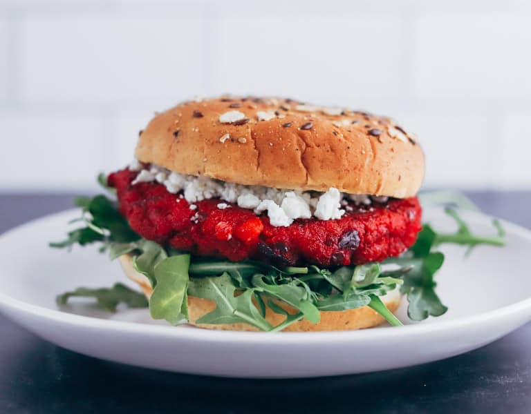 beet burger topped with arugula, goat cheese, and a seeded bun sits on a plate