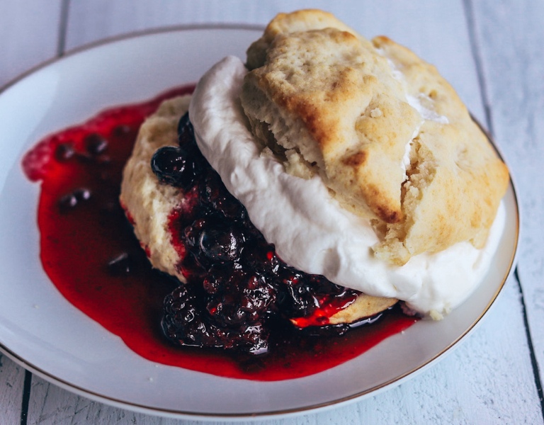 buttermilk biscuit filled with berry compote and whipped cream on a fine china plate