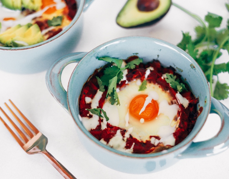 chilaquiles rojos casserole in a small blue dutch oven topped with an egg and avocado