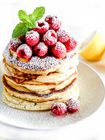lemon ricotta pancakes are stacked and topped with raspberries and dusted with powdered sugar