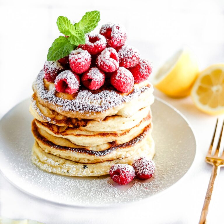 lemon ricotta pancakes are stacked and topped with raspberries and dusted with powdered sugar