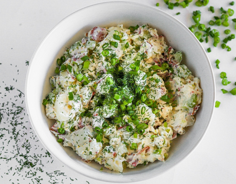 white bowl with red potato salad and toppings of diced green onion and dill weed